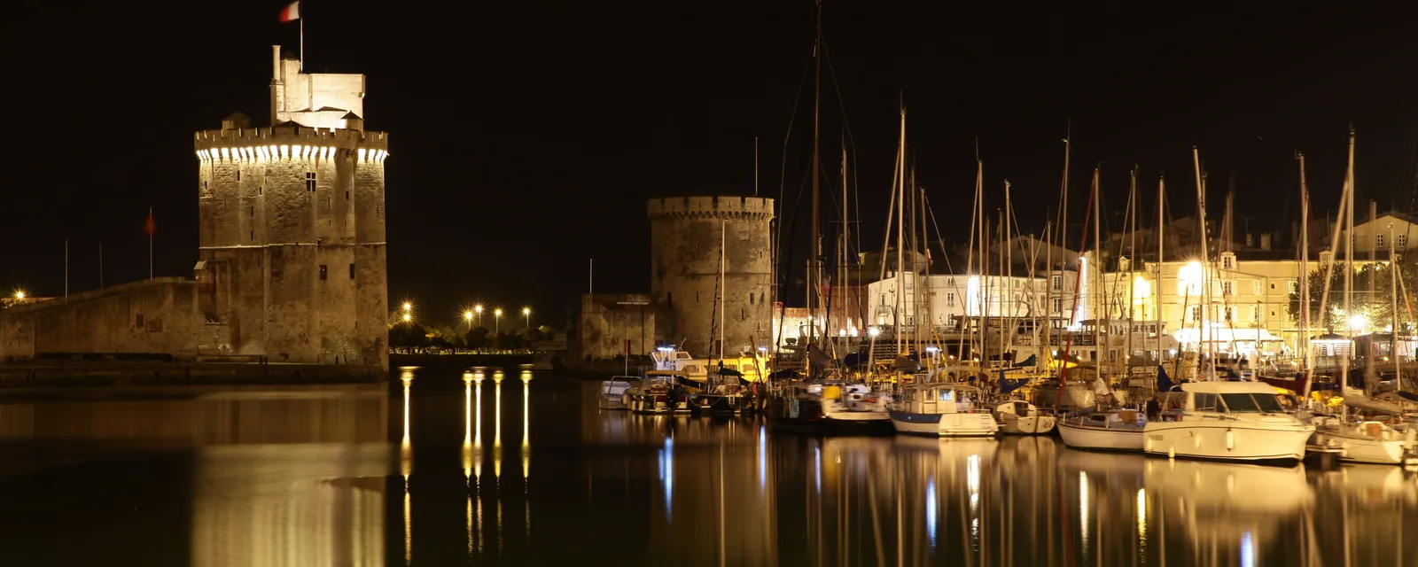 Vue nocturne du Vieux-Port de La Rochelle avec les tours médiévales illuminées se reflétant dans l'eau